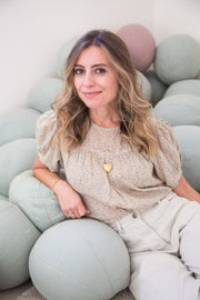 A woman sits on a pile of balls, smiling at the camera, wearing a gold heart pendant.